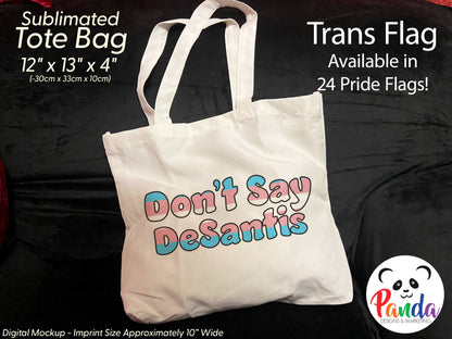 Photo of a white tote bag on a black velvet count. The back has "Don't Say DeSantis" in trans pride flag colors with black outline of fun shaped text